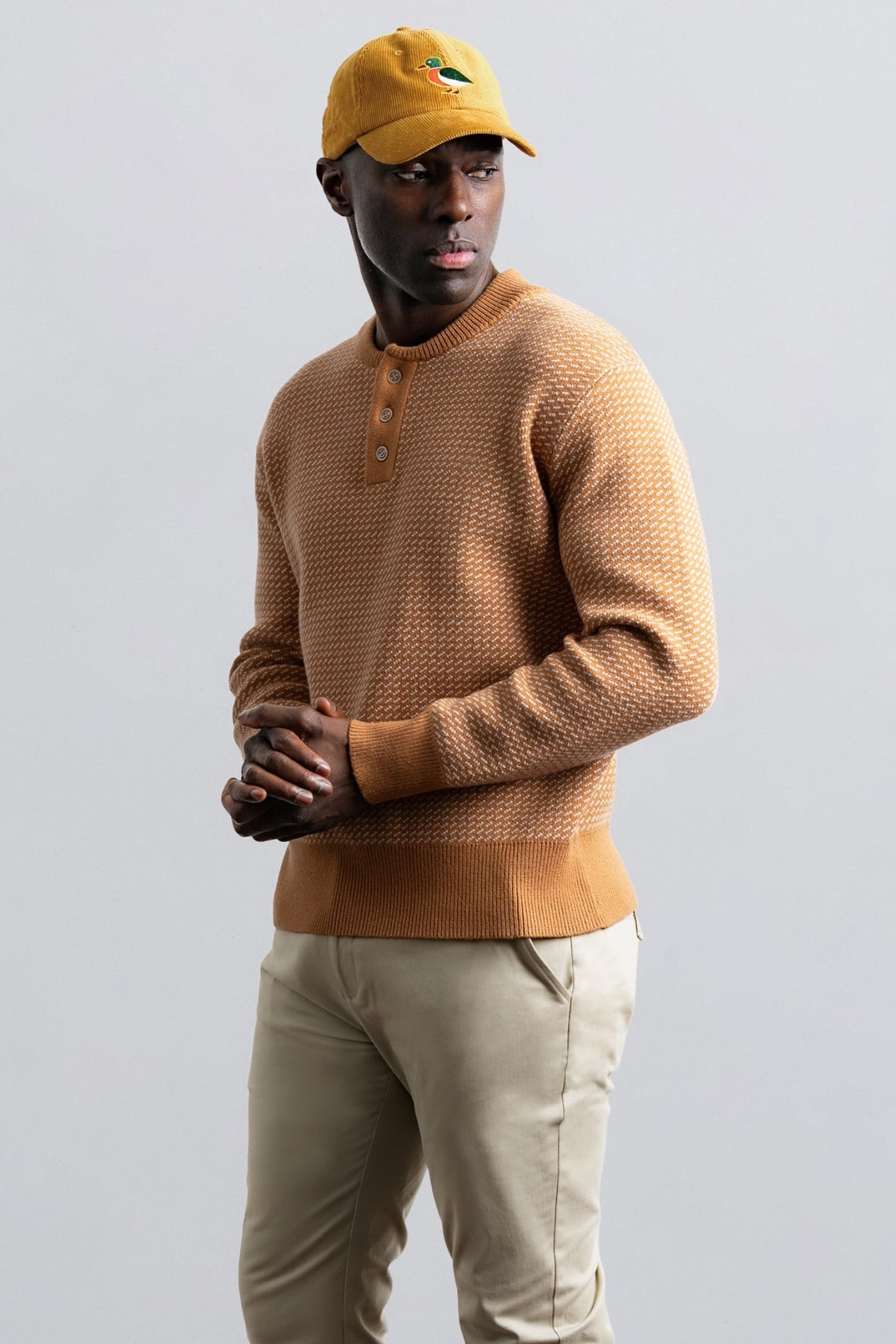 Man wearing a brown sweater and yellow cap against a gray background
