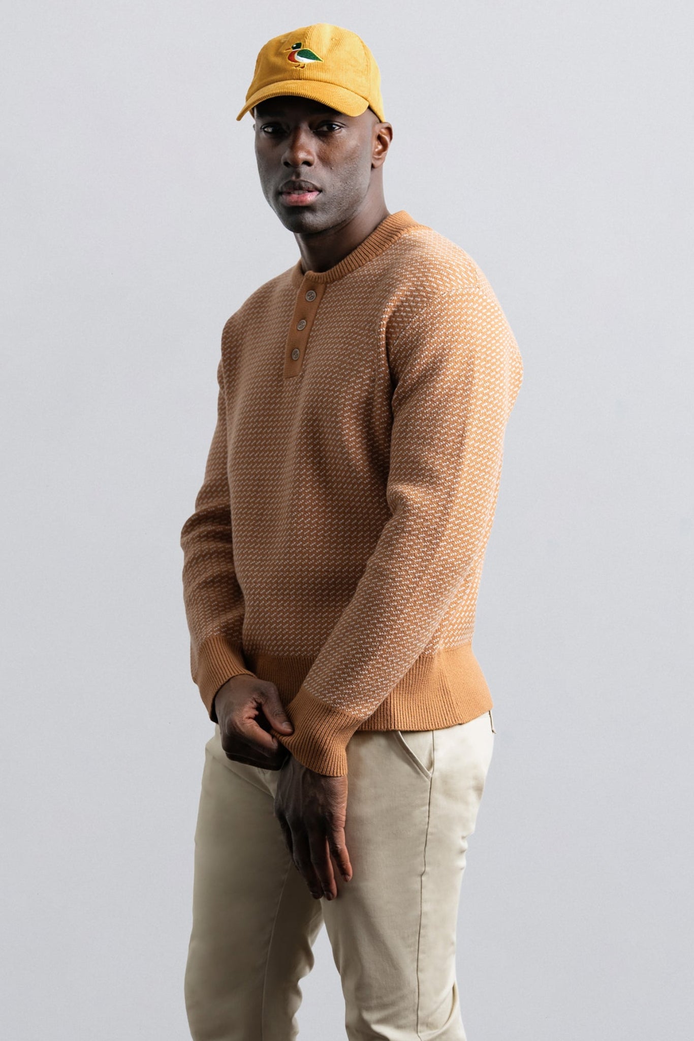 Man wearing a brown sweater and yellow cap against a plain background