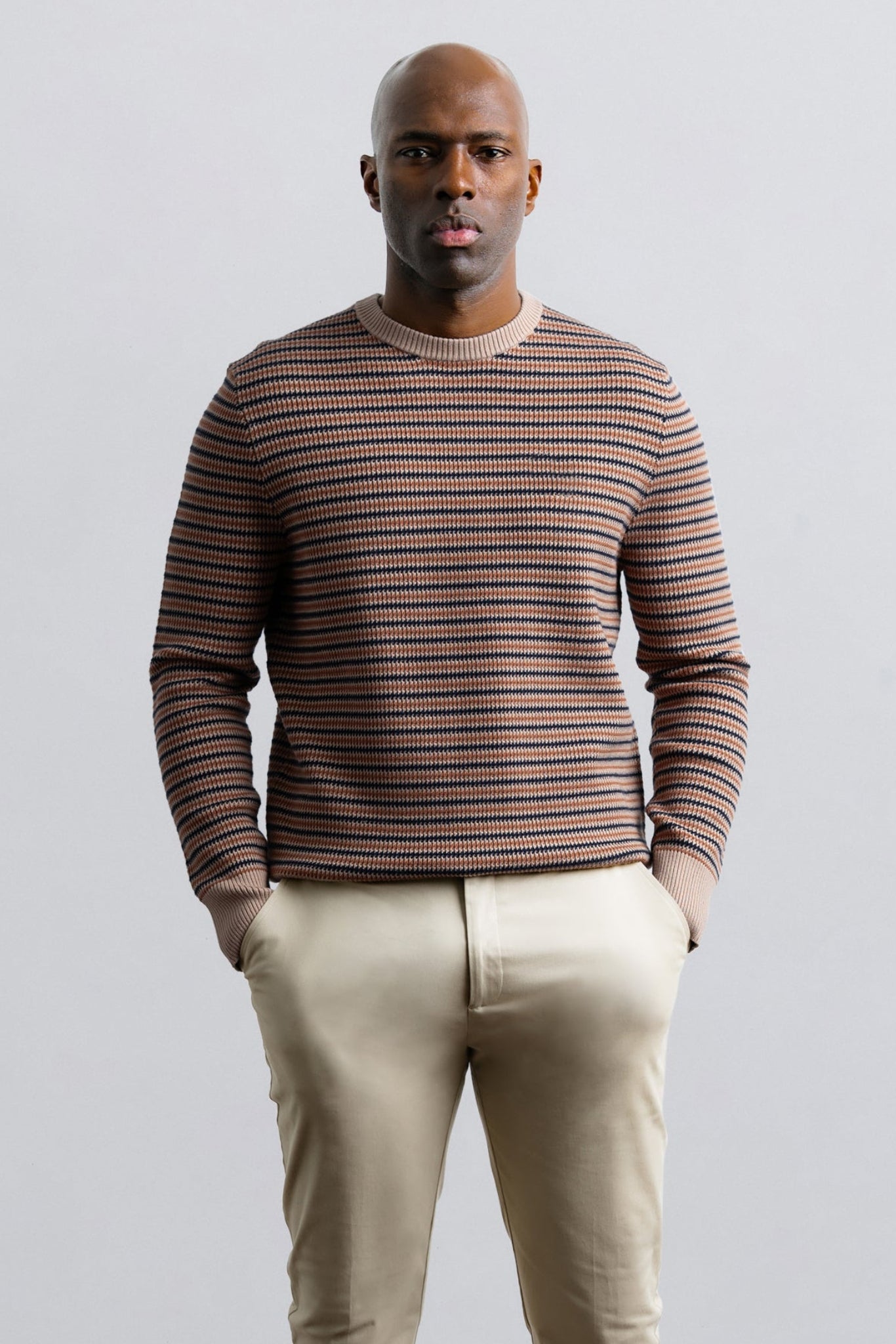 Man wearing a striped sweater and beige pants against a plain background