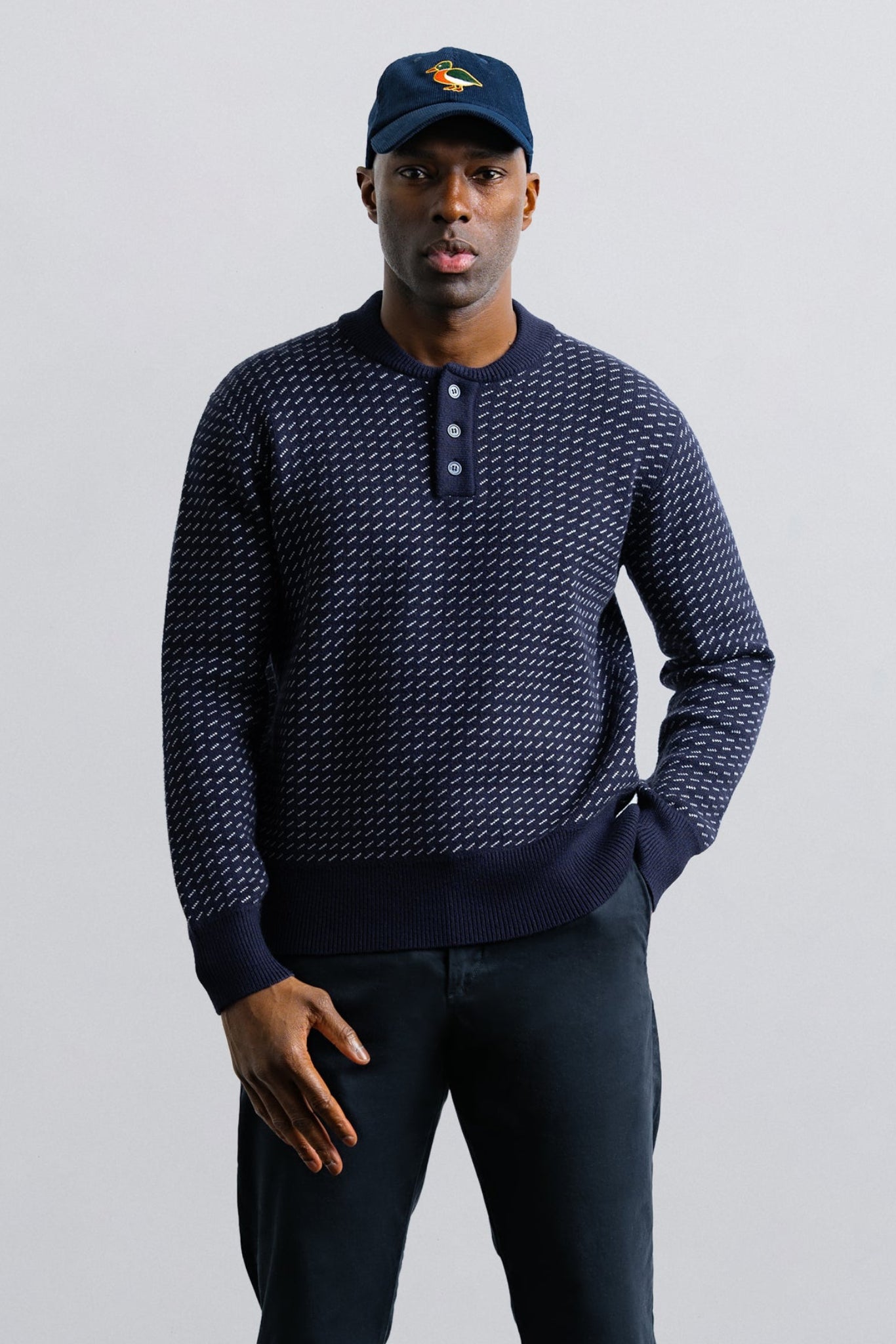 Man wearing a navy patterned sweater and cap on a light gray background