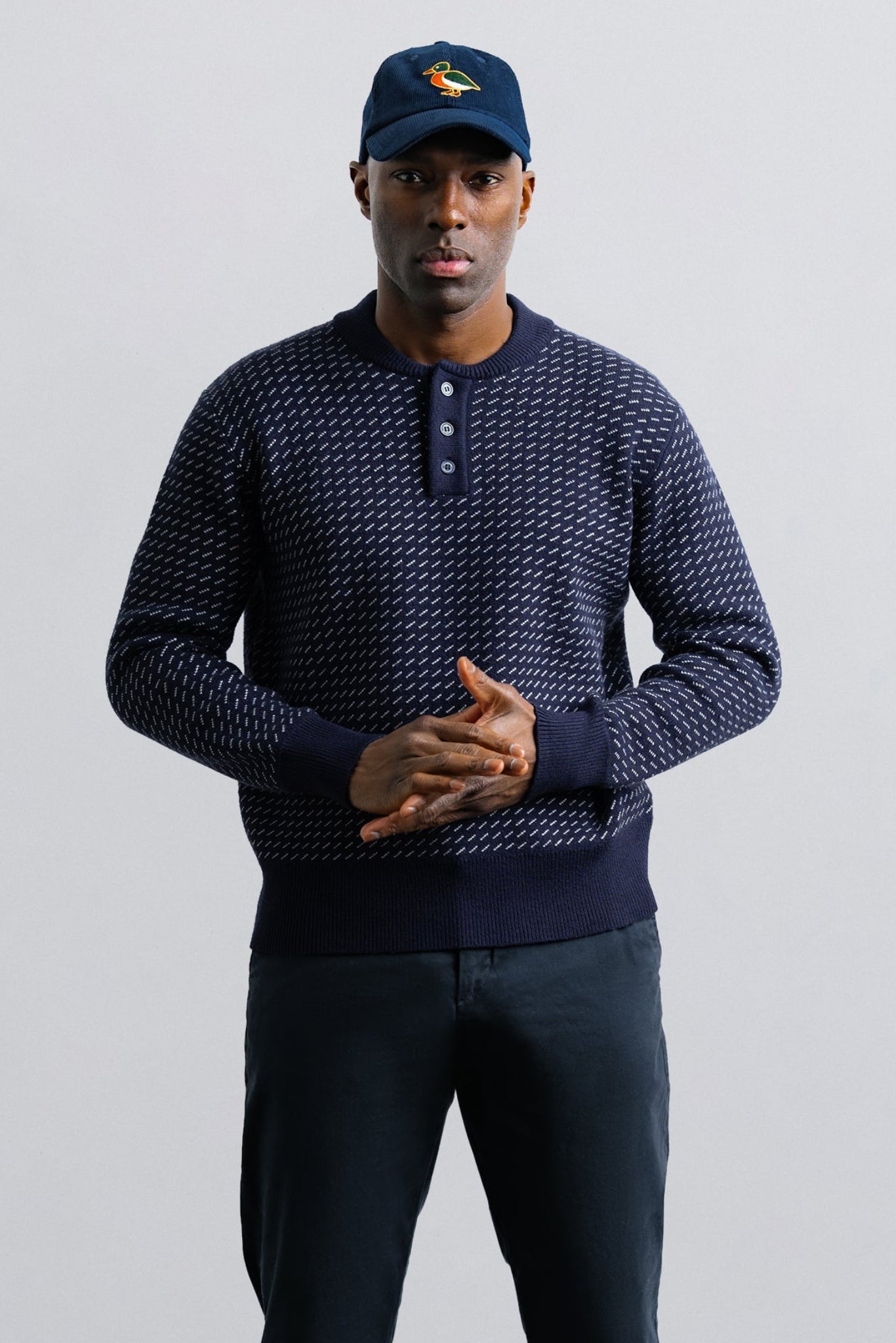 Man wearing a navy patterned sweater and cap on a light gray background