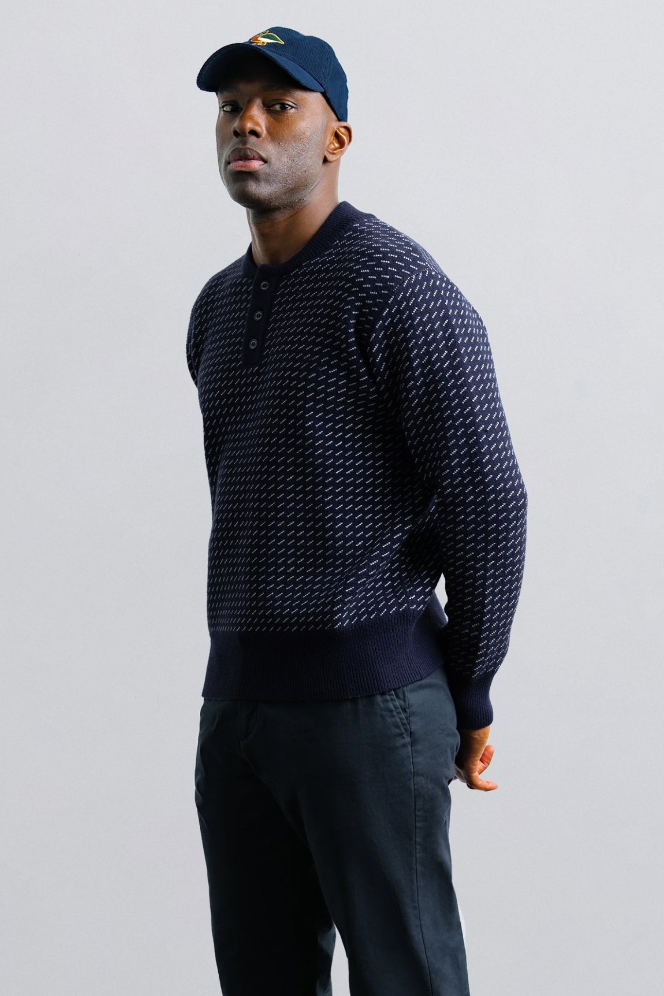 Man wearing a dark patterned sweater and cap against a plain background