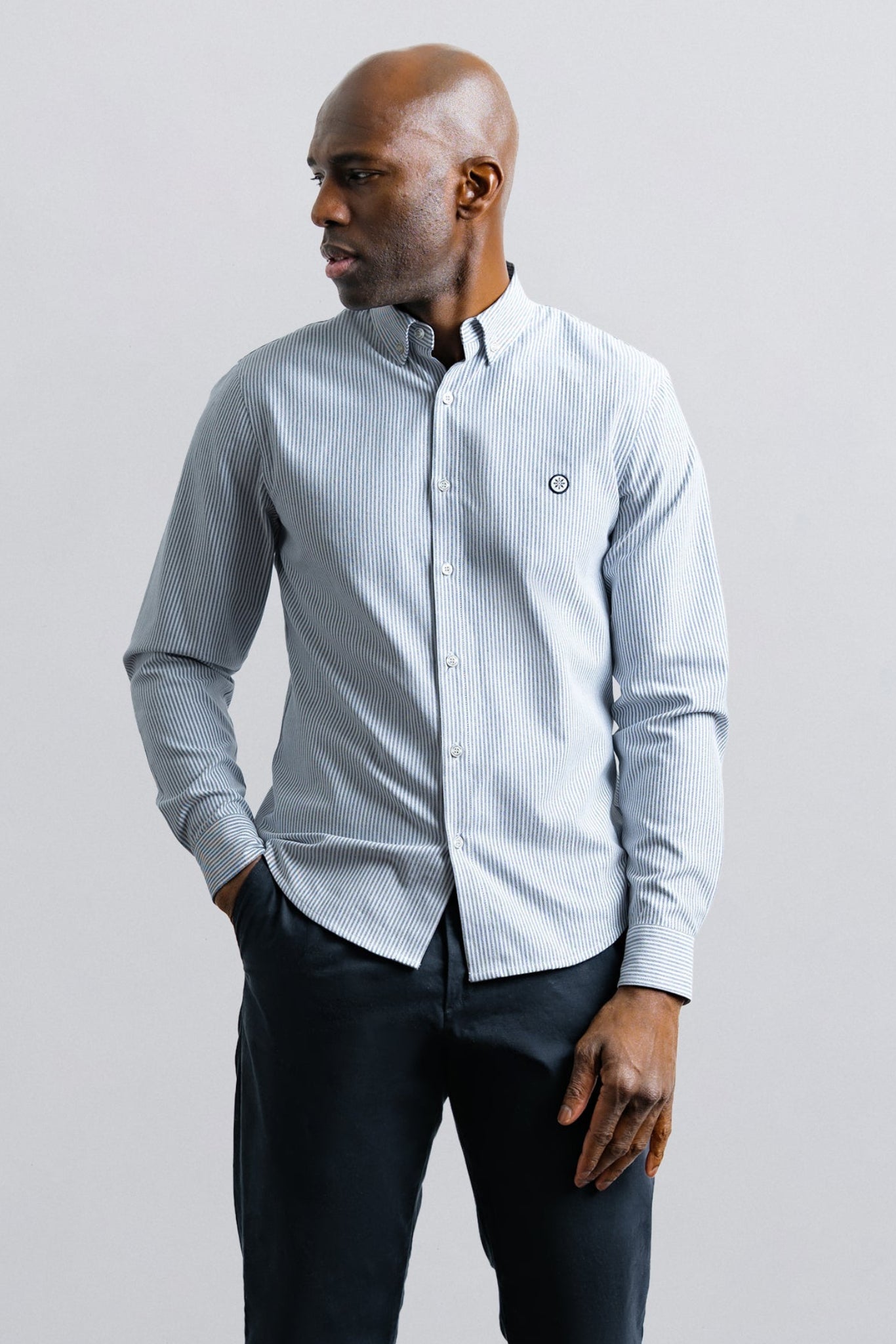 Man wearing a light blue button-up shirt and dark pants against a plain background