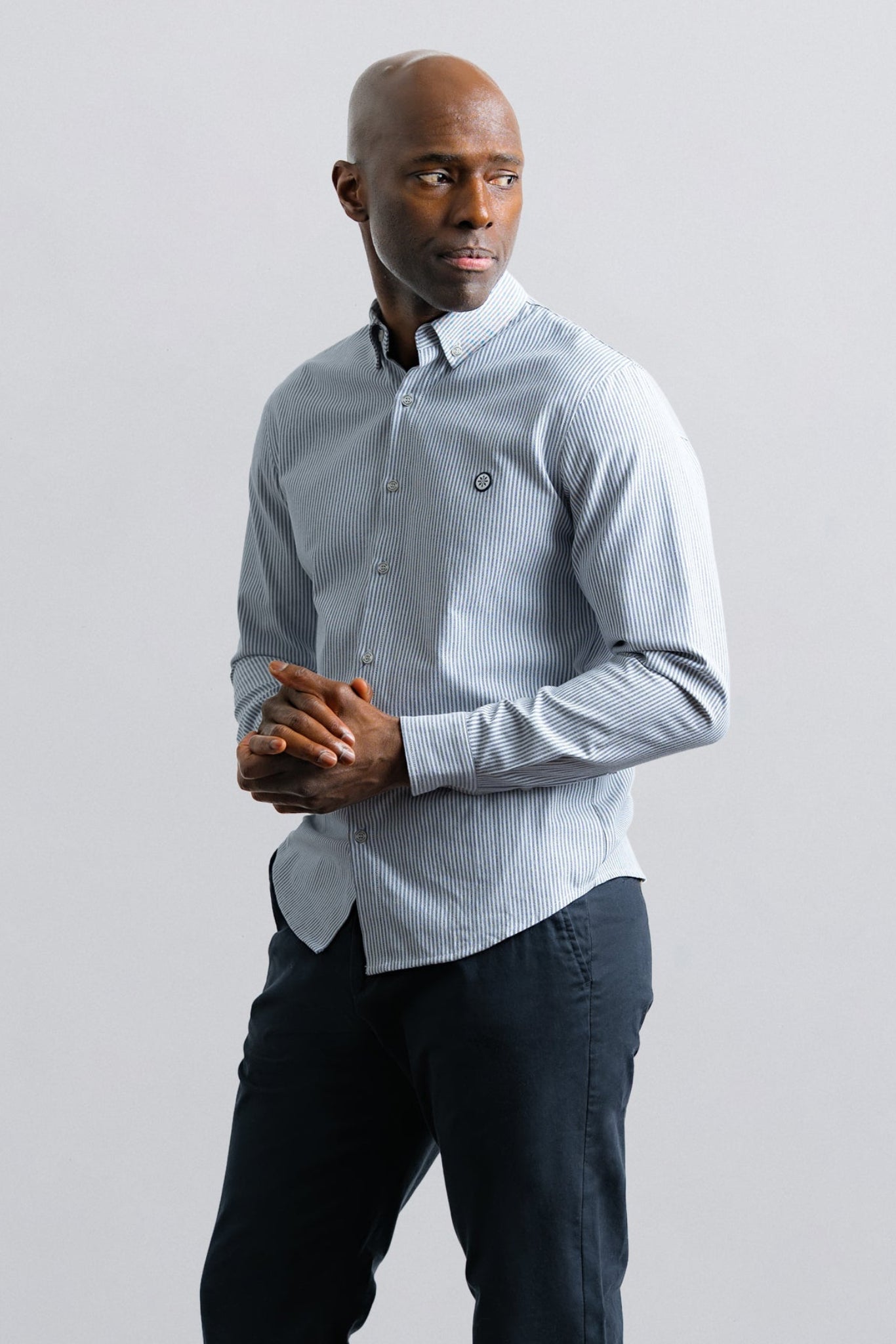 Man wearing a light blue shirt and dark pants against a plain background
