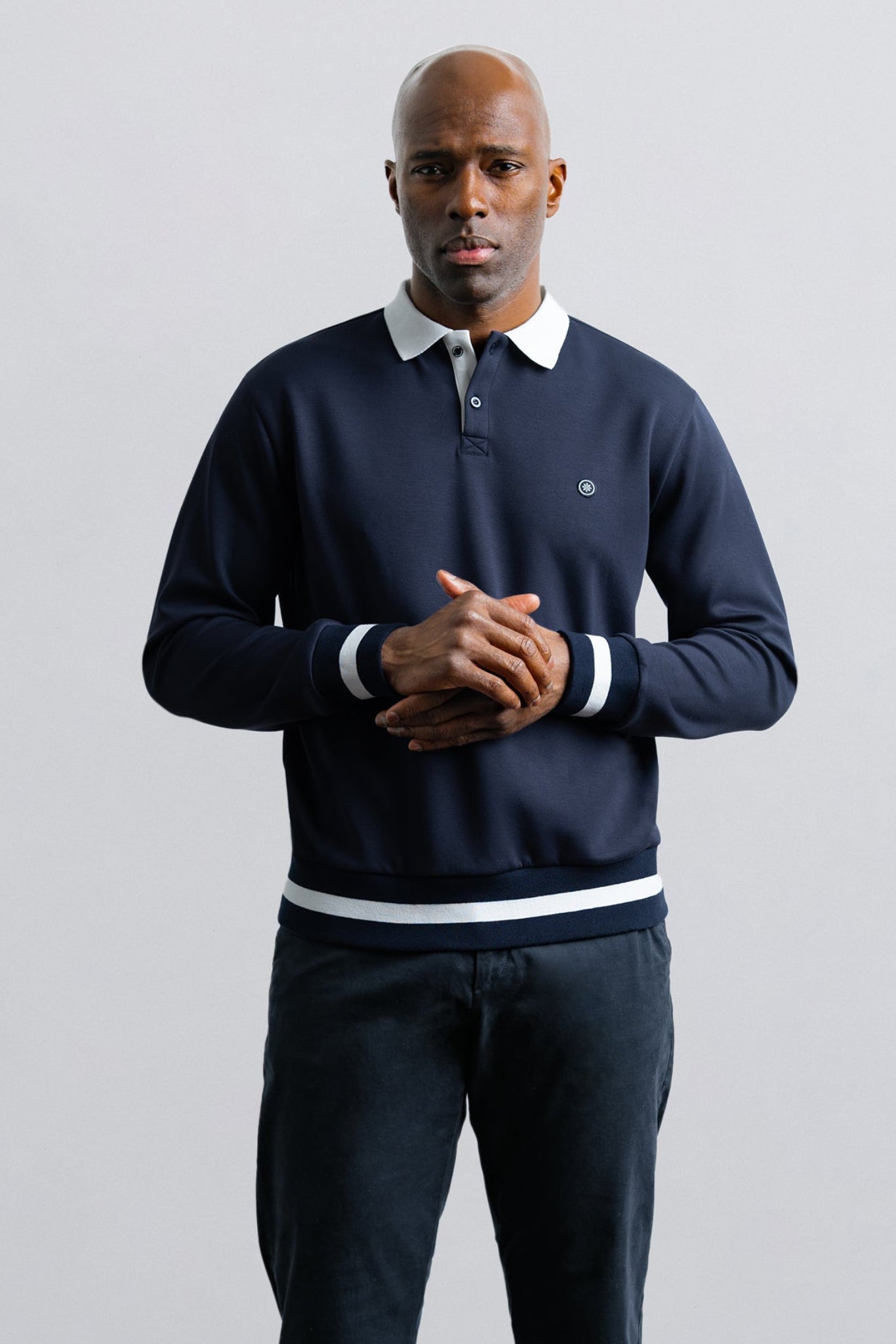 Man wearing a navy sweater with white collar and cuffs on a light gray background