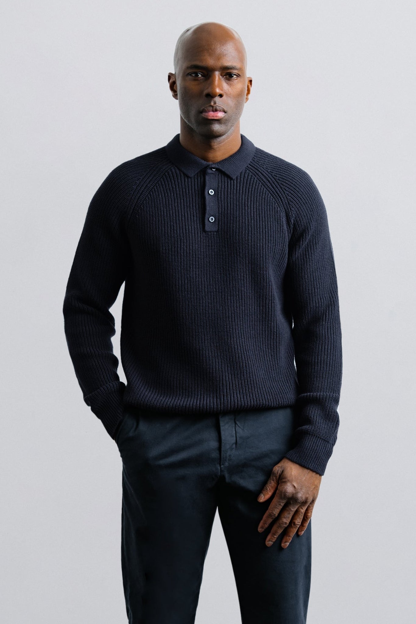 Man wearing a dark blue sweater and pants against a light gray background