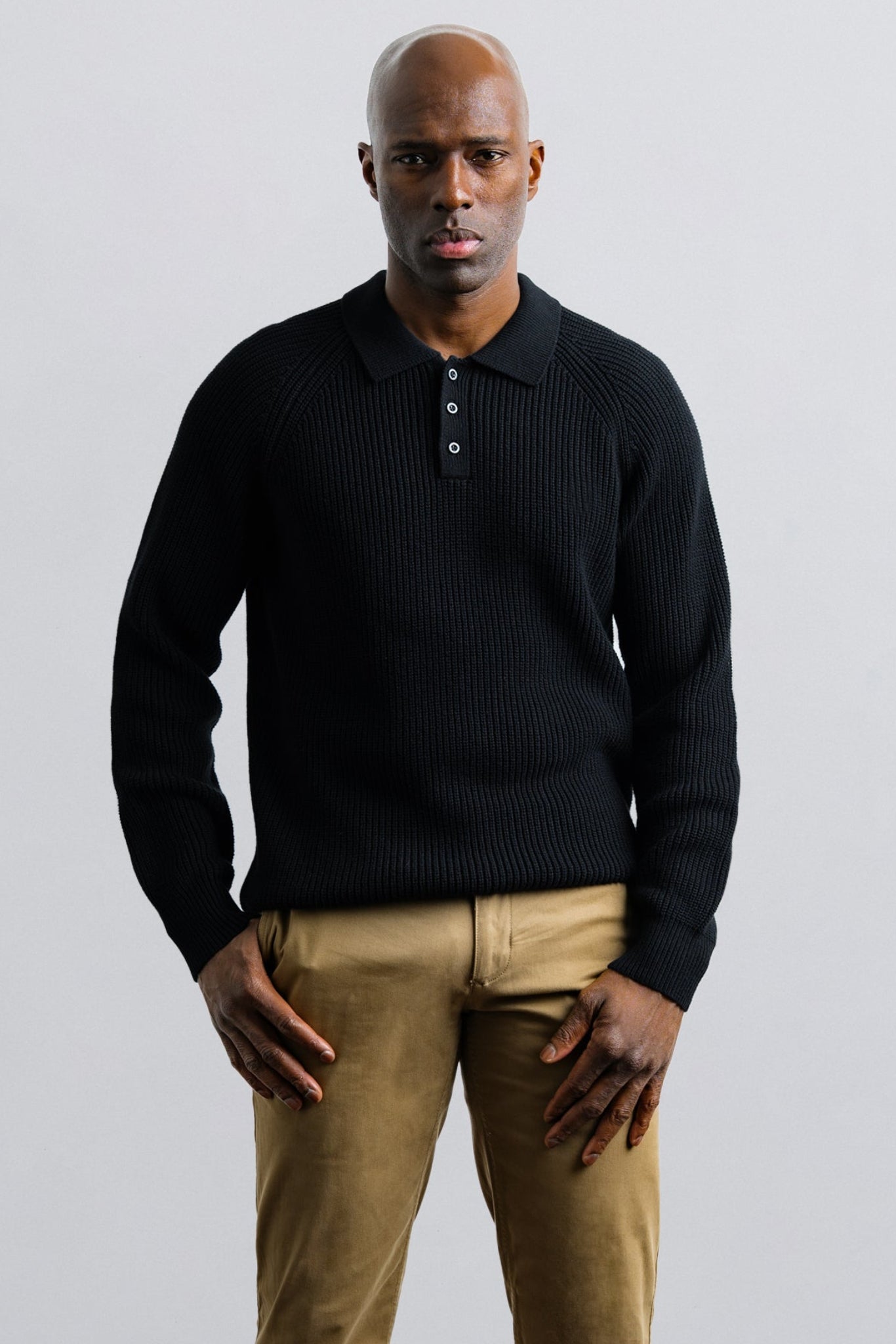 Man wearing a black sweater and beige pants against a plain background