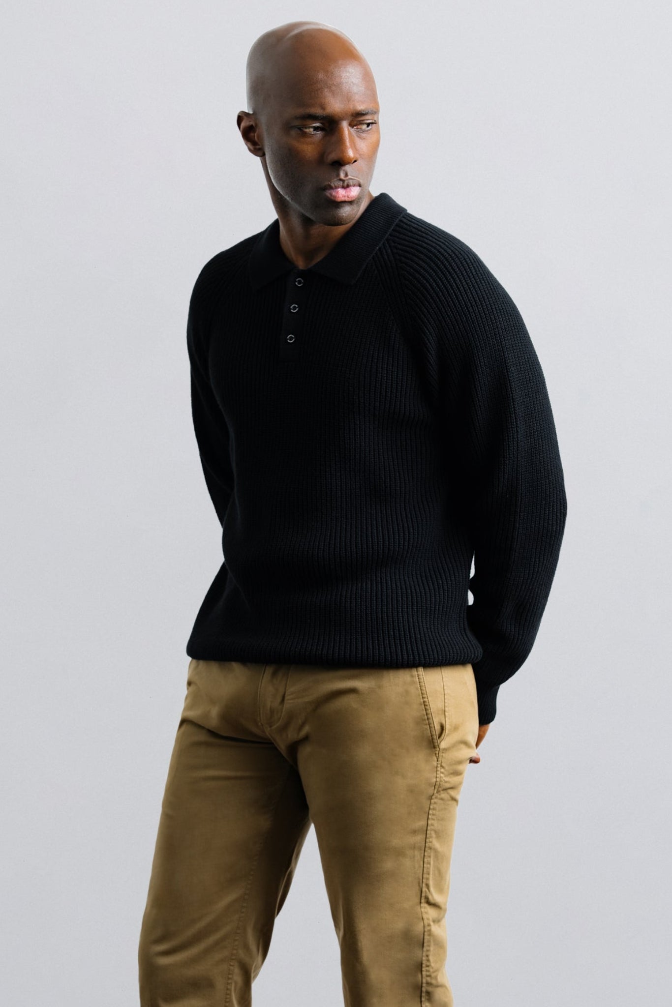 Man wearing a black sweater and beige pants against a light gray background