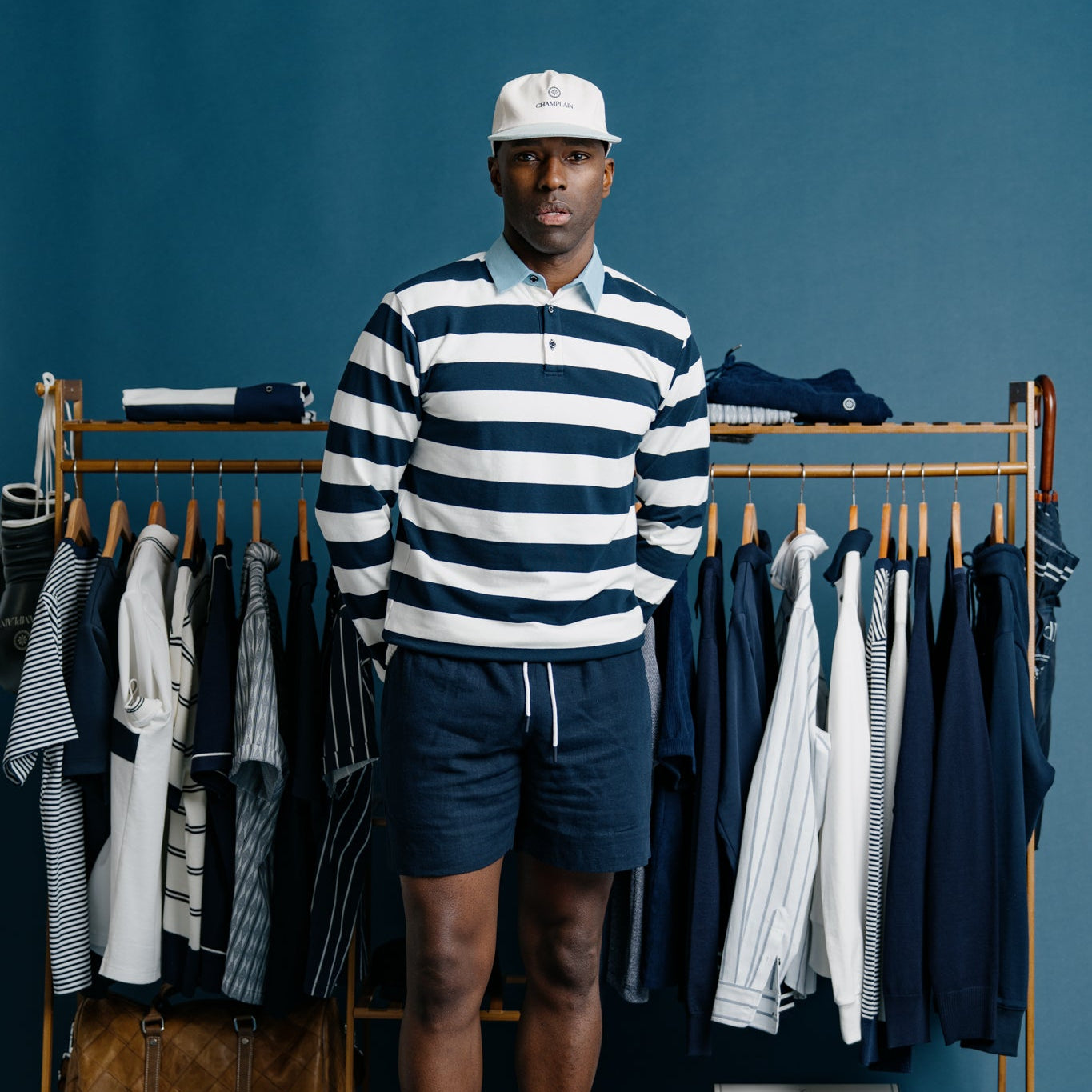 Man standing in front of a clothing rack with blue and white striped shirt and shorts on a blue background