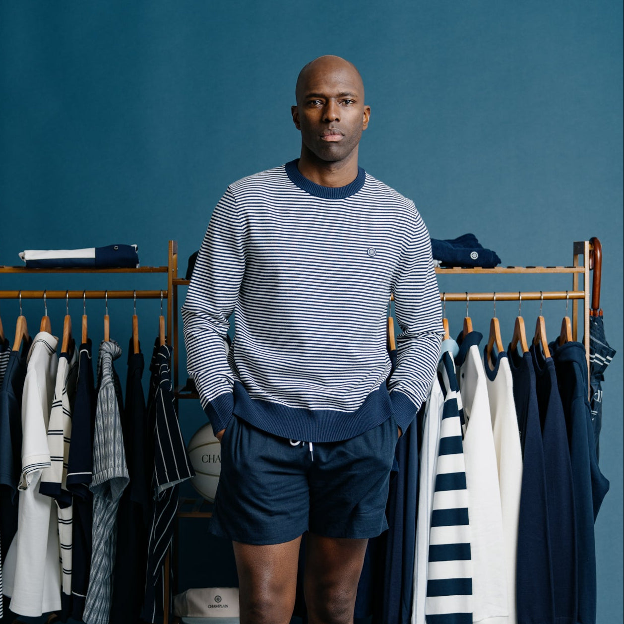 Man standing in front of a clothing rack with various garments on a blue background