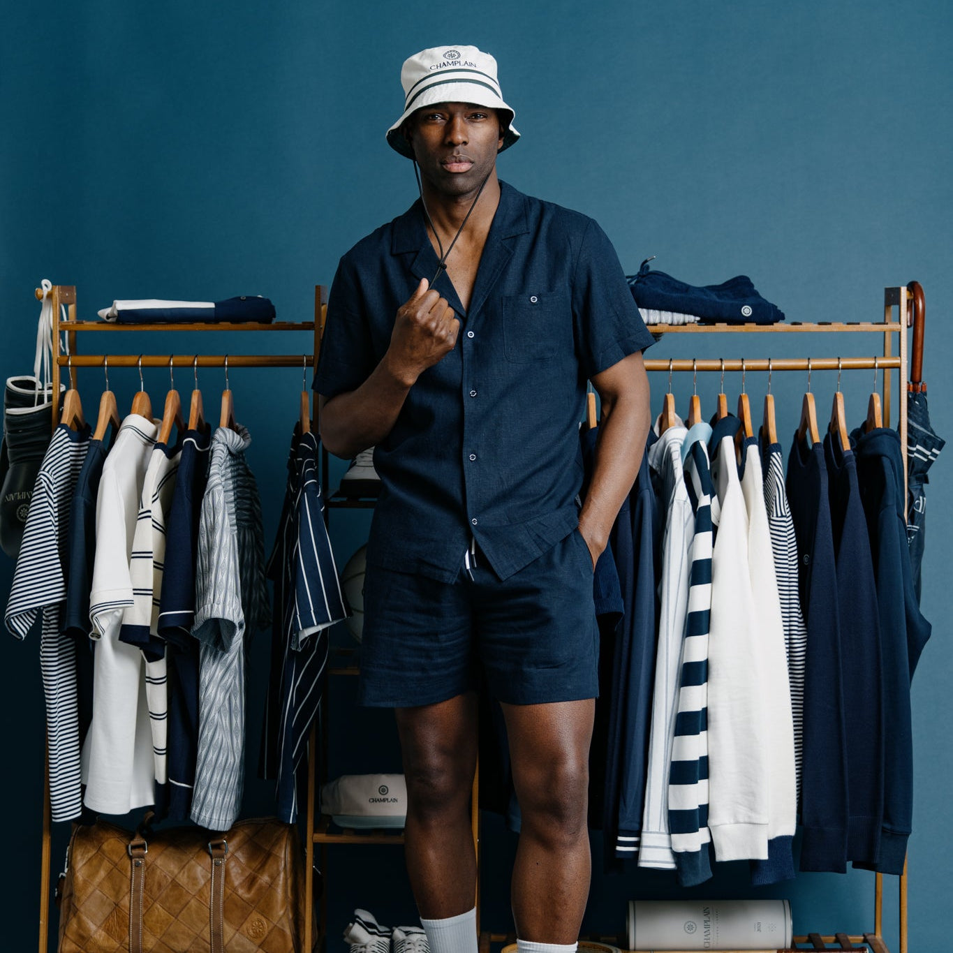 Man in navy outfit standing in front of a clothing rack with blue background