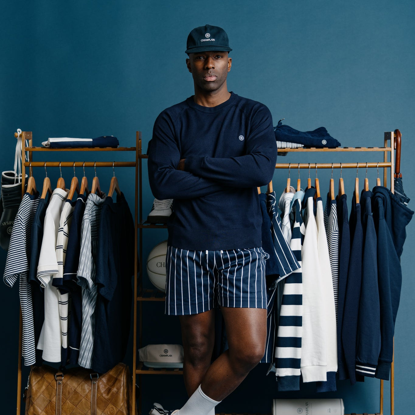 Man standing in front of a clothing rack with blue and white striped shirts against a blue wall.