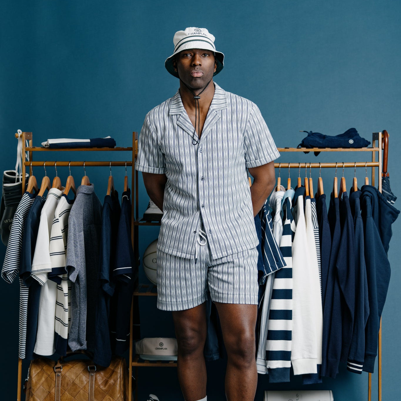 Man in a striped outfit standing in front of a clothing rack with various garments on a blue background