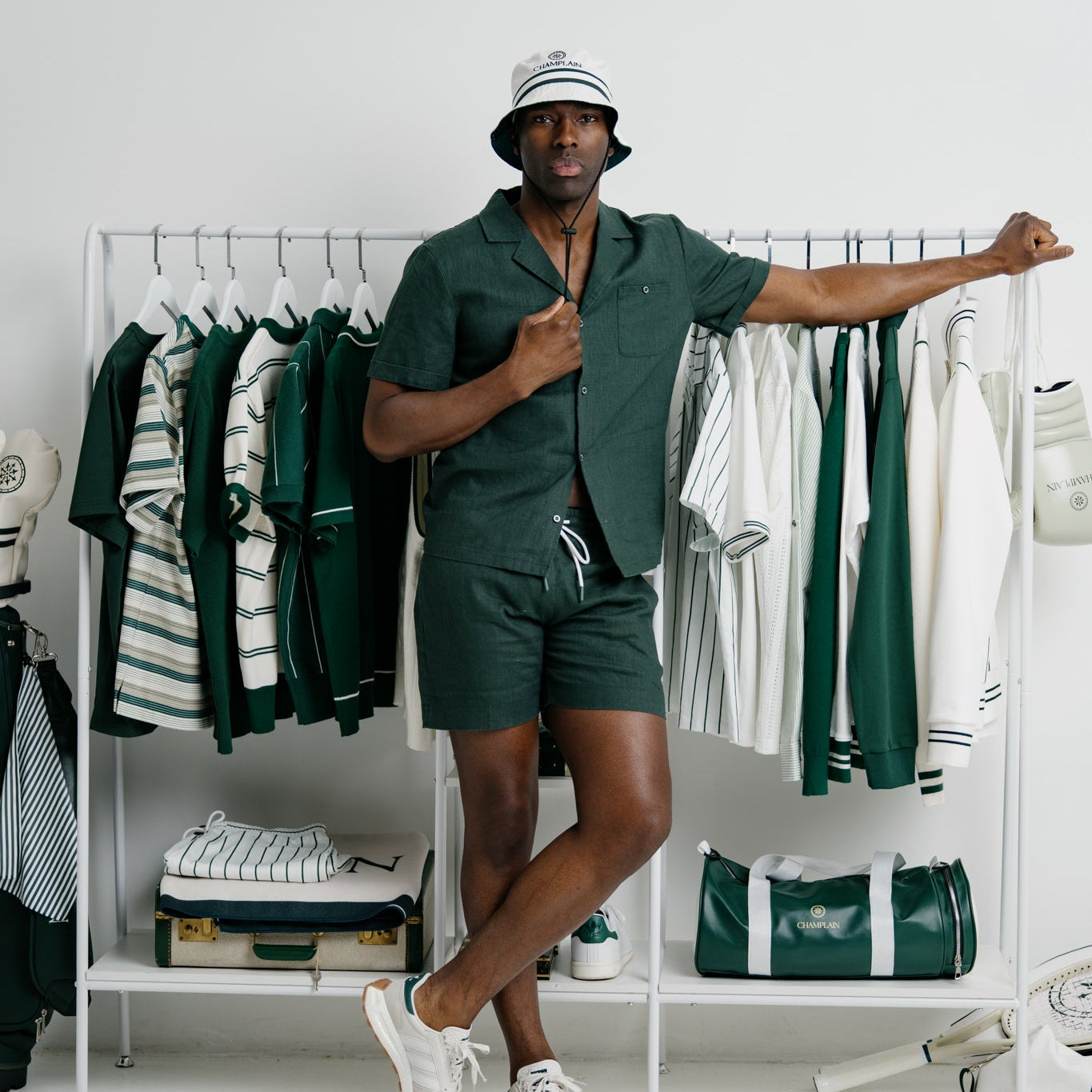 Man in green outfit standing next to a rack of clothes in a room.