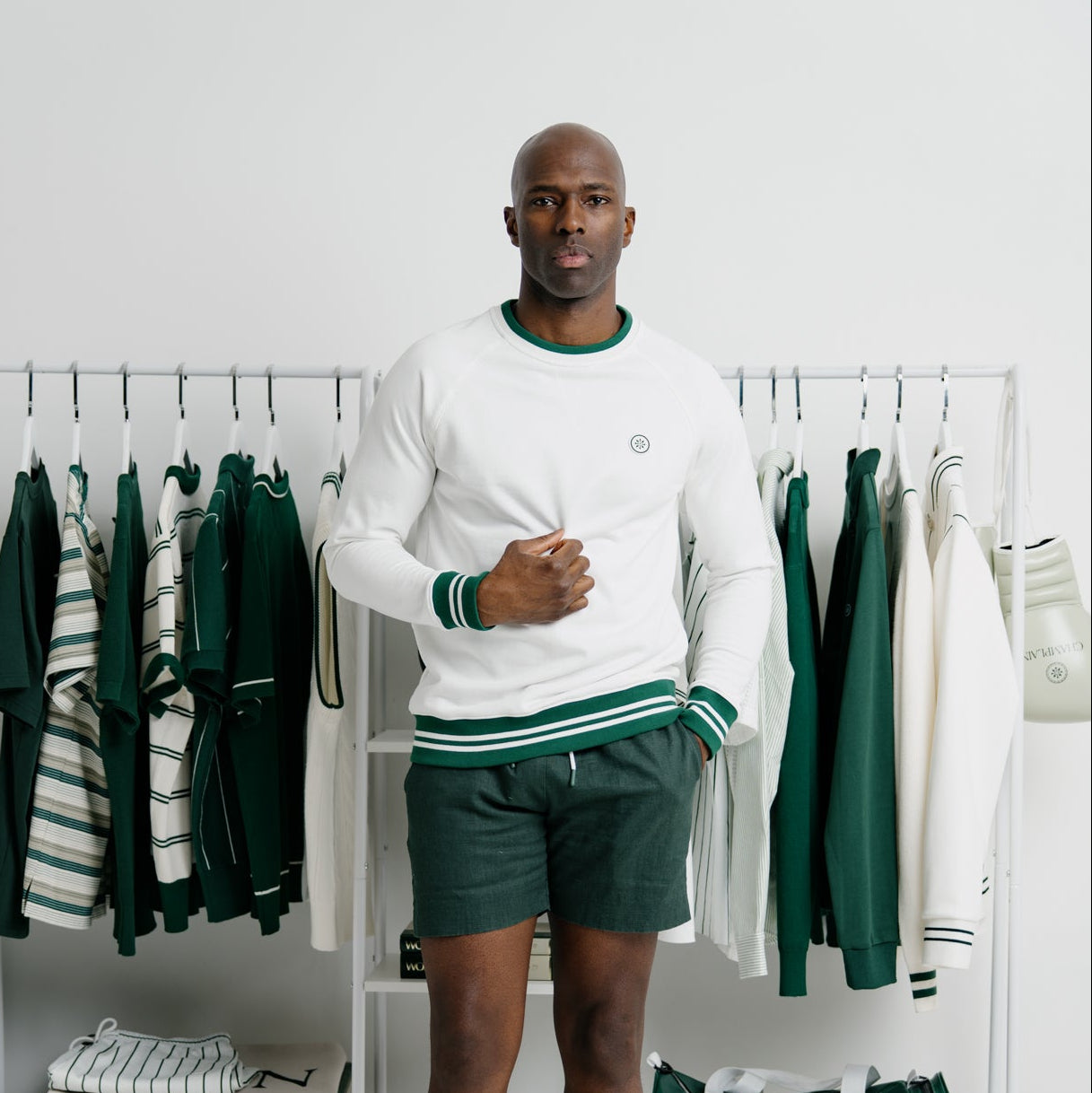 Man standing in a room with clothing racks and green and white outfits.