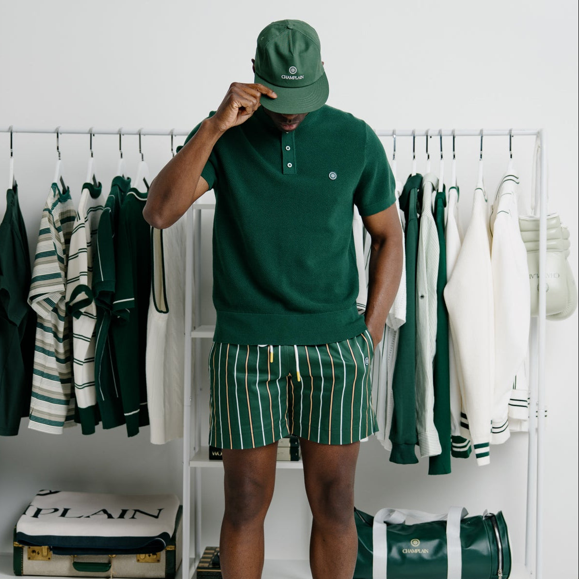 Person wearing a green outfit standing in front of a clothing rack with various garments.