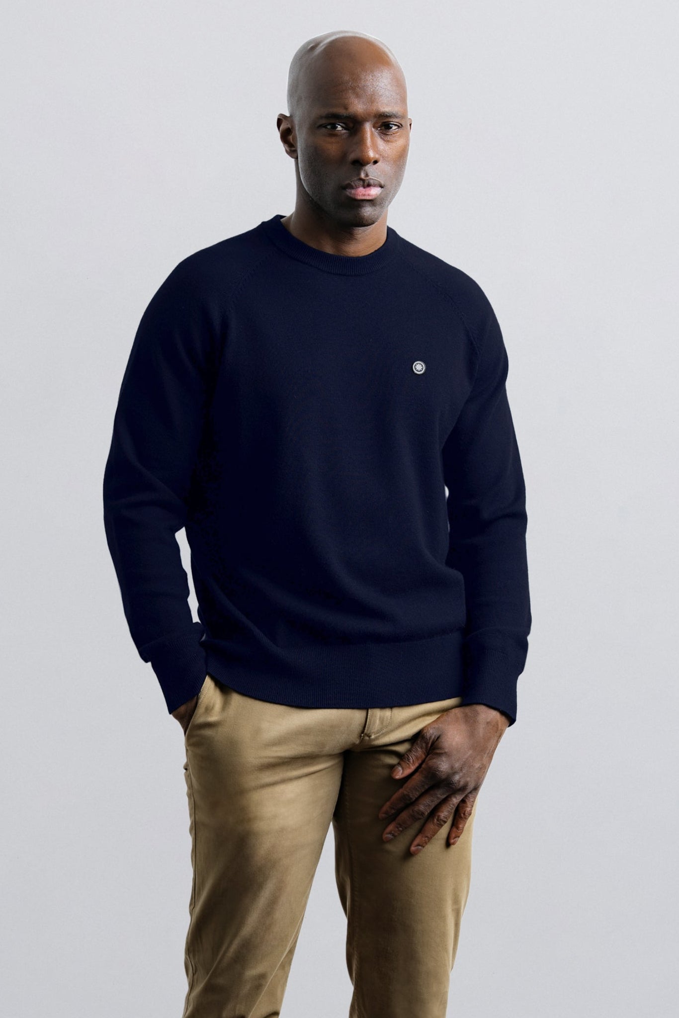 Man wearing a black sweater and beige pants against a plain background